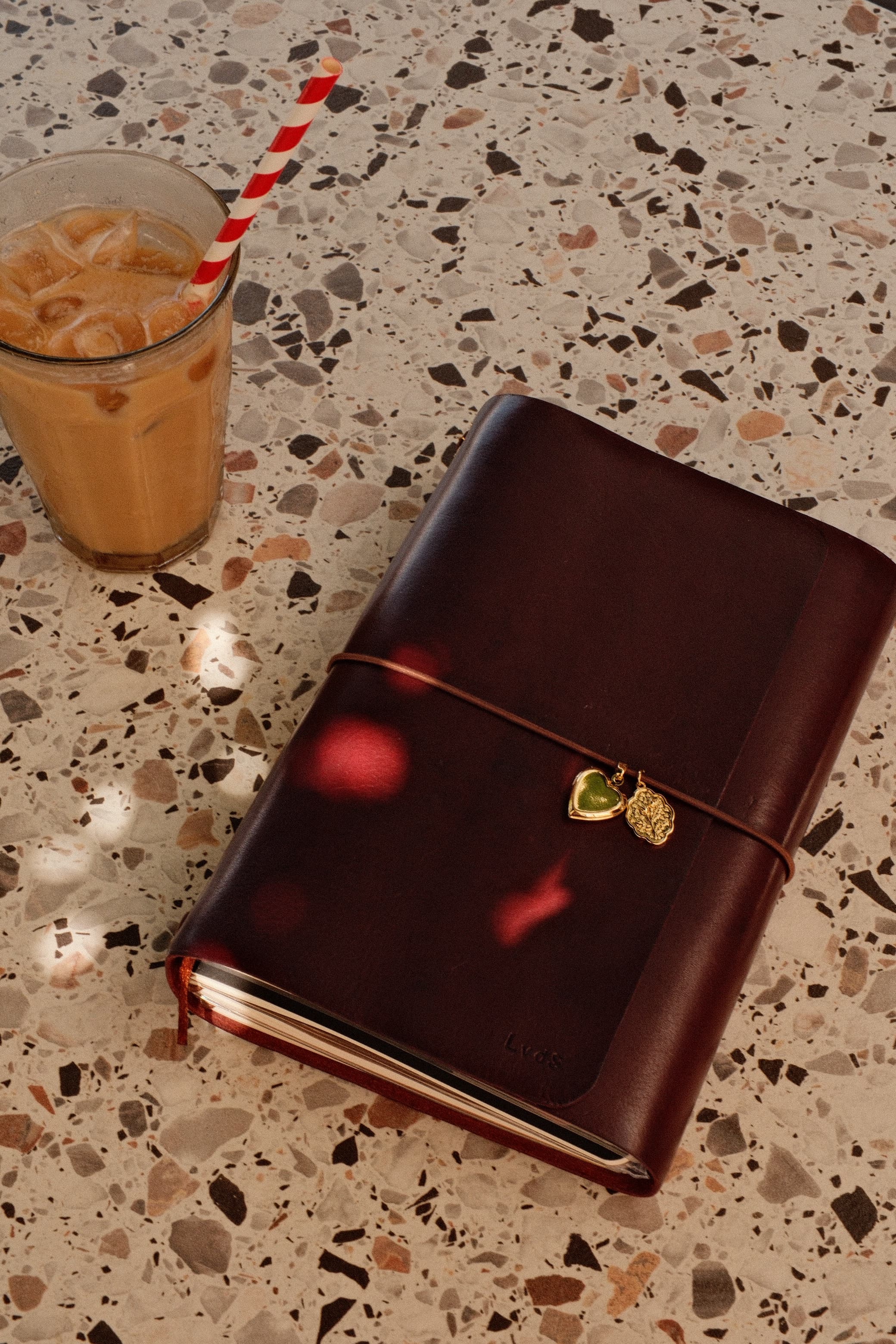 Een bordeauxrode leren journal met gouden bedels naast een ijskoffie